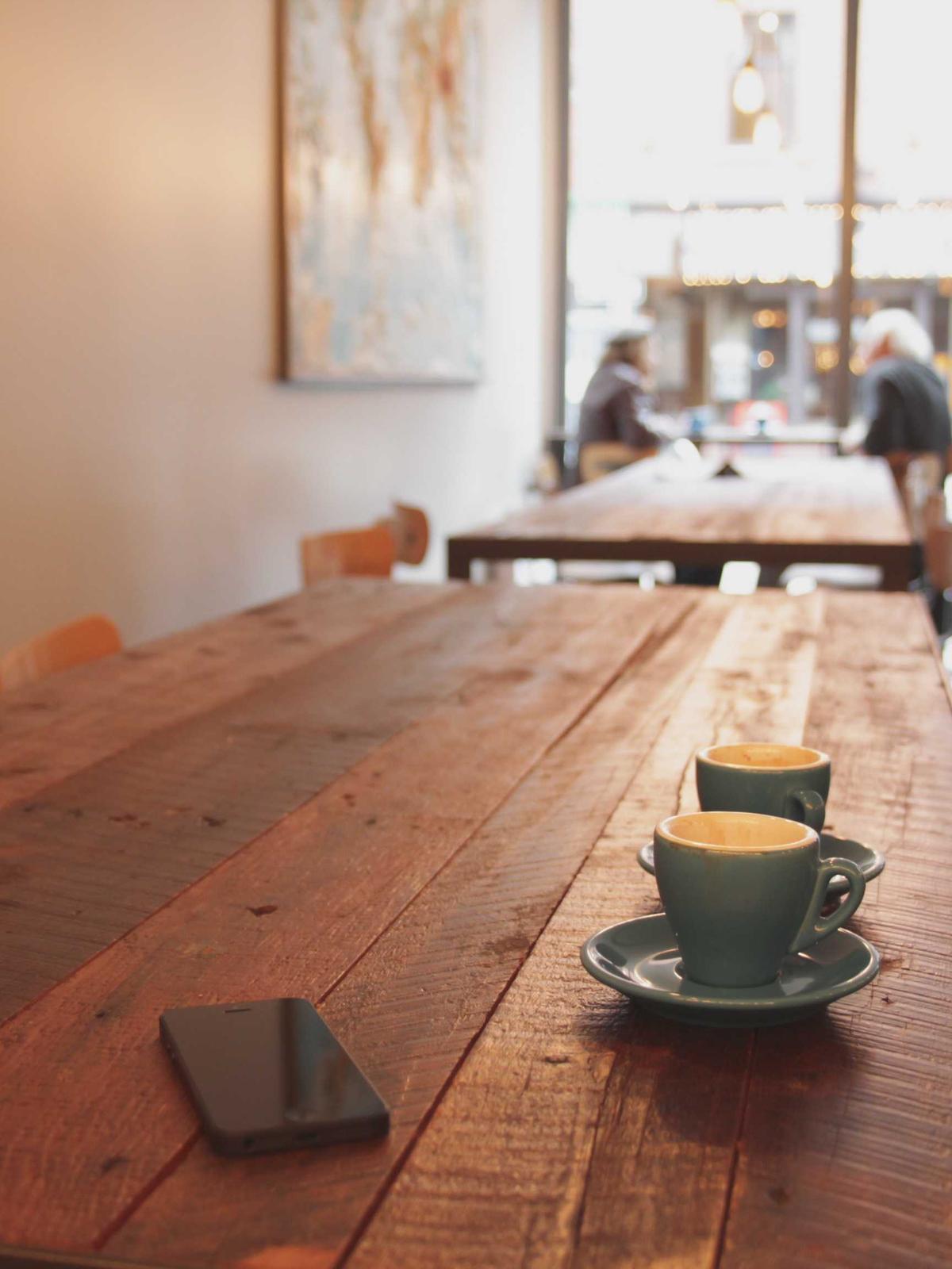 Zwei Tassen Kaffee auf einem langen Holztisch in einem hellen Café