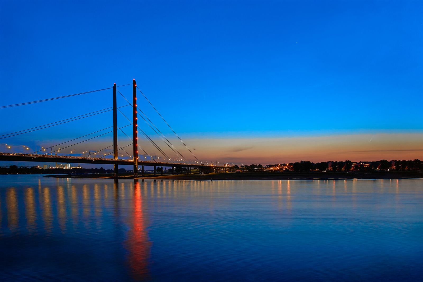 Die Rheinkniebrücke in Düsseldorf zur blauen Stunde, die Lichter spiegeln sich im Rhein