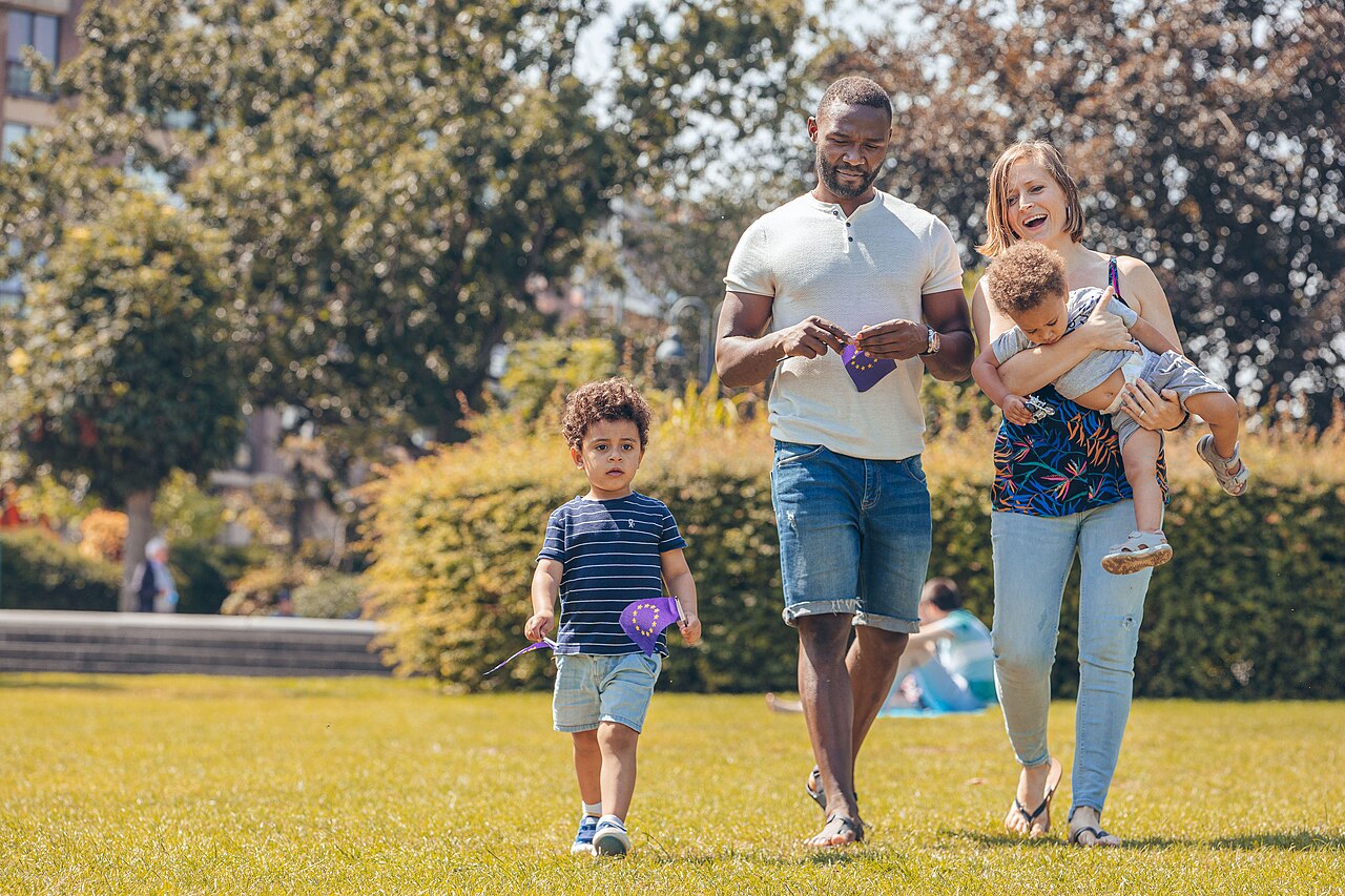 Eltern mit zwei kleinen Kindern laufen lachend über eine Wiese im Park