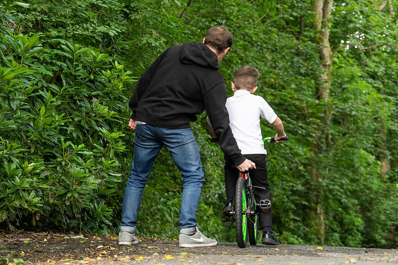 Ein Vater hält das Fahrrad seines Sohnes fest, der gerade Radfahren lernt