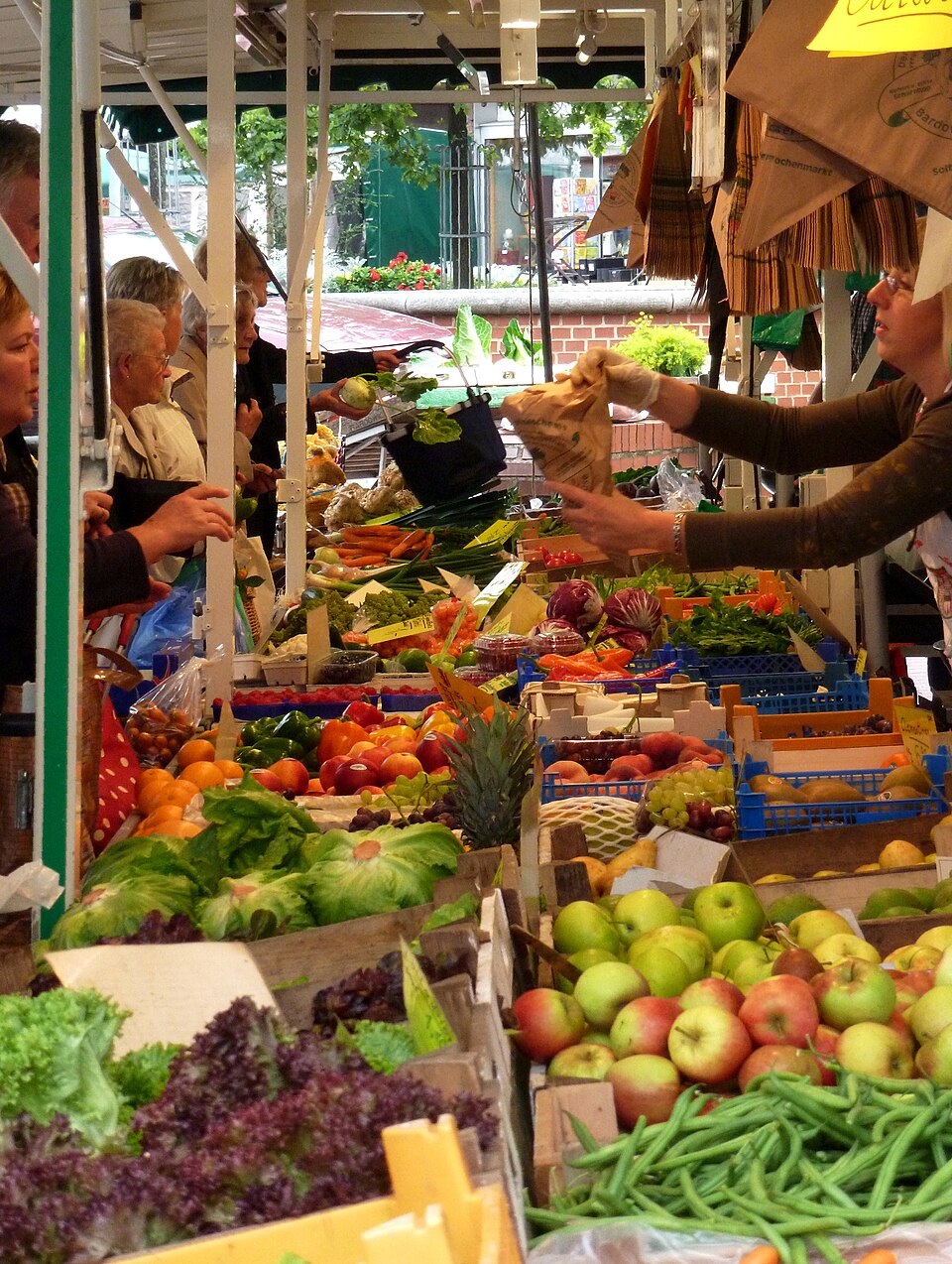 Marktstand auf einem Wochenmarkt: Eine Händlerin reicht einer Kundin eine Tüte über Obst und Gemüse