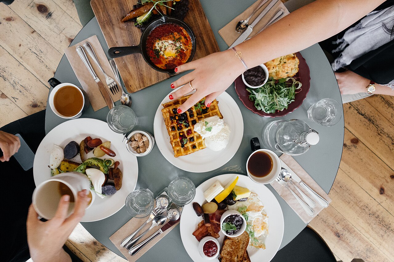 Von oben gesehen: ein runder Tisch mit Frühstück, Kaffee und vielen Händen