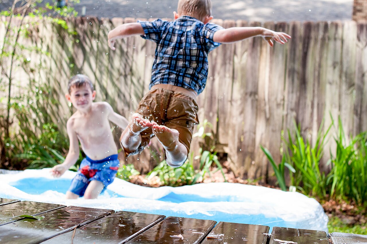 Zwei Jungen springen im Garten in ein aufblasbares Planschbecken