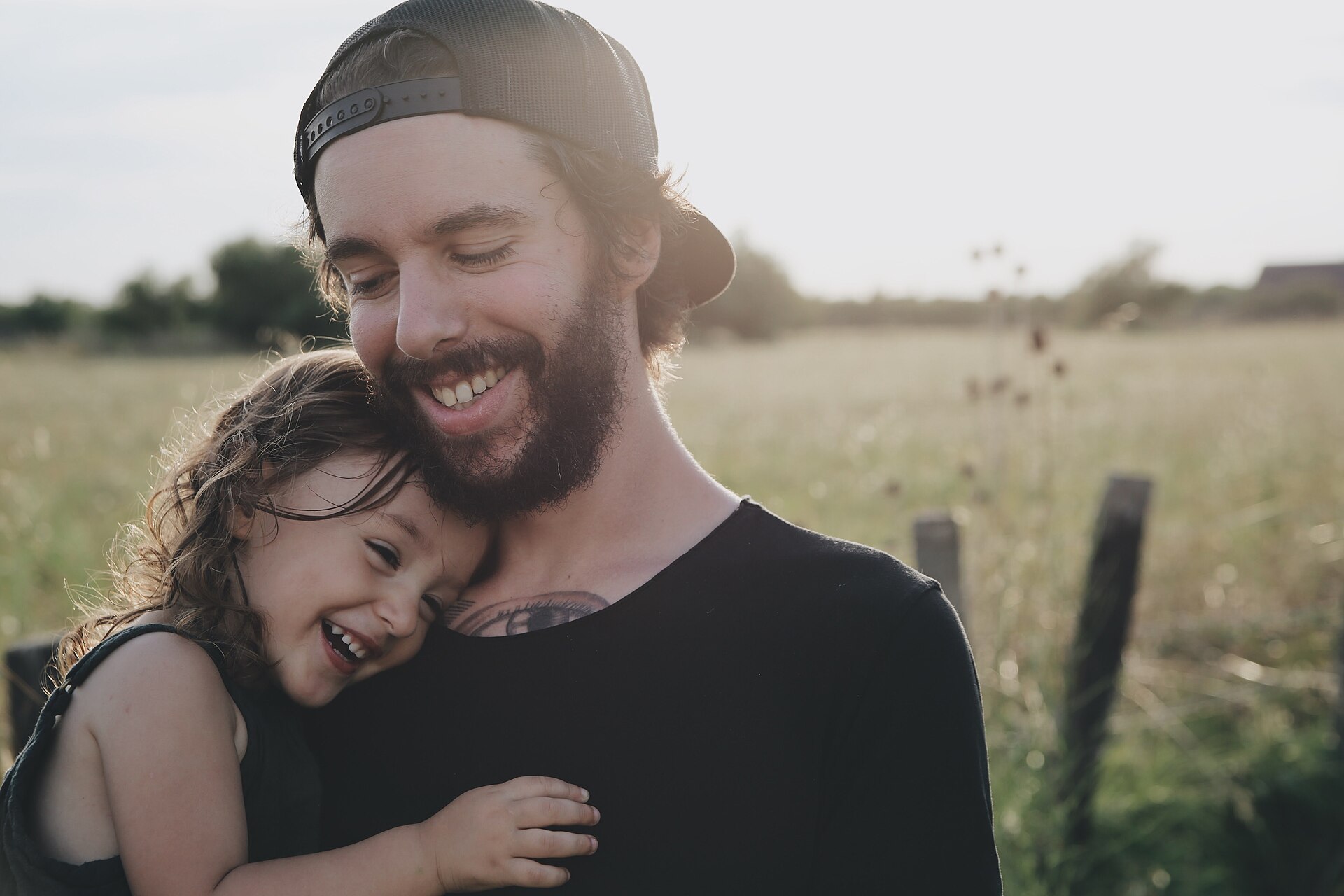 Ein Vater hält lachend seine kleine Tochter im Arm, dahinter ein Sommerfeld