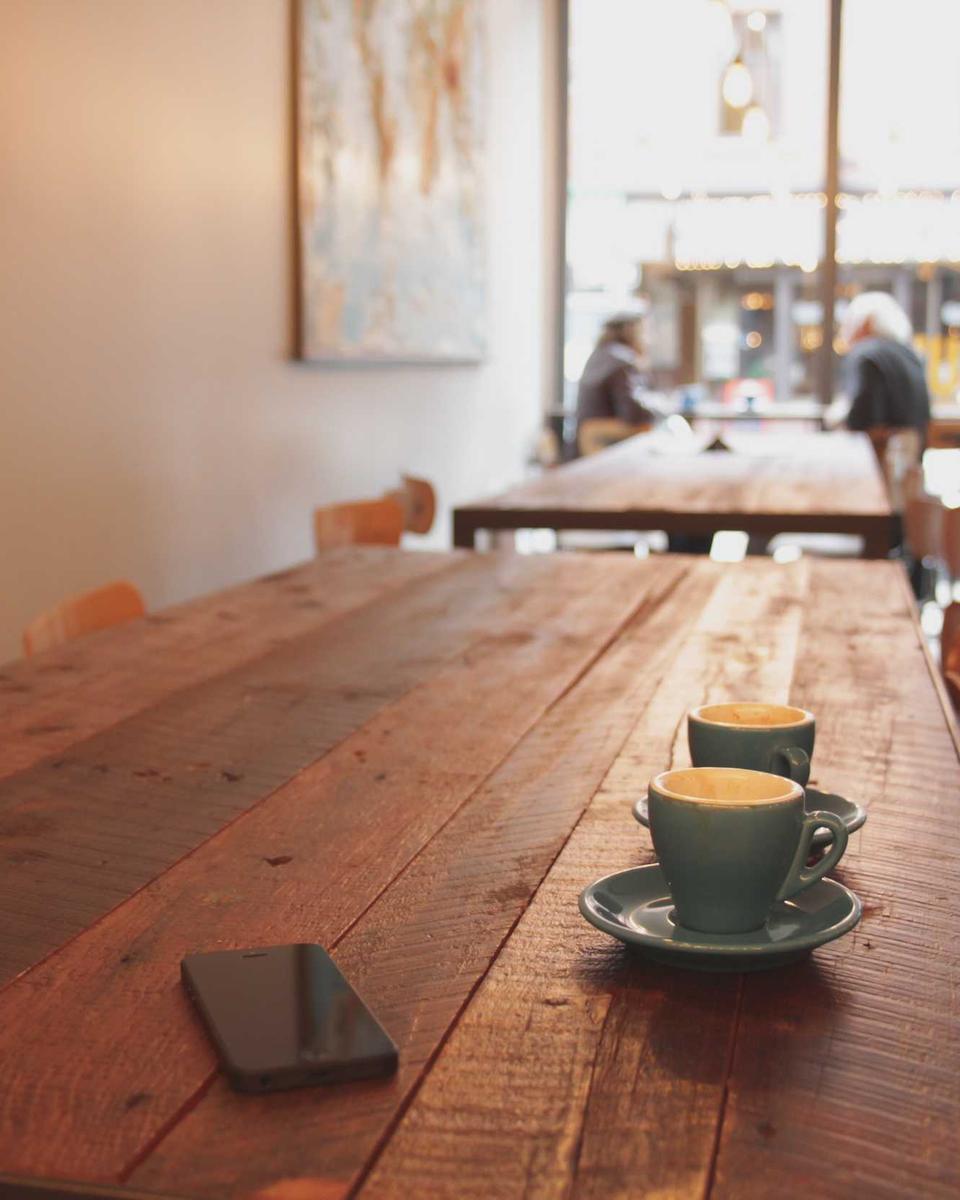 Zwei Tassen Kaffee auf einem langen Holztisch in einem hellen Café