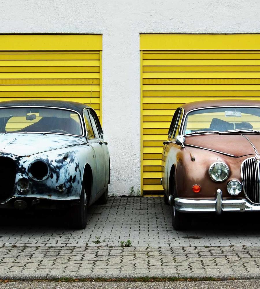 Zwei alte Jaguar-Limousinen vor gelben Garagentoren
