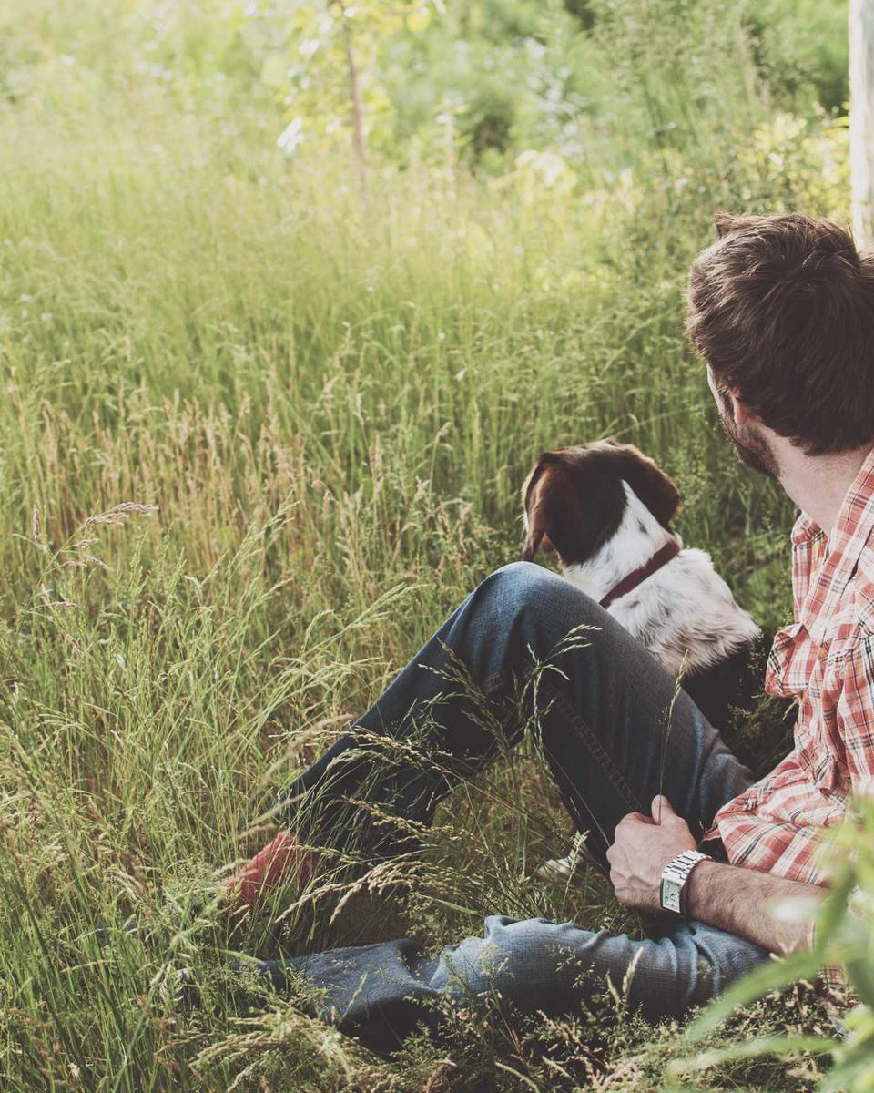 Ein Mann sitzt mit seinem Hund im hohen Gras