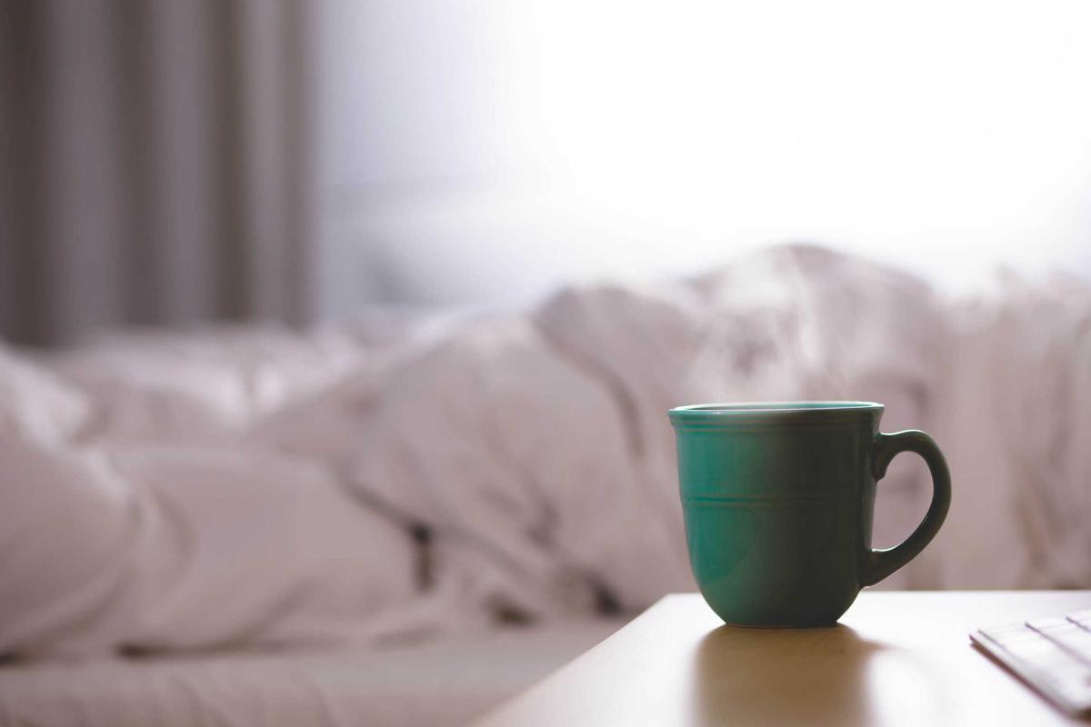 Eine grüne Tasse auf dem Nachttisch neben zerwühlter weißer Bettwäsche
