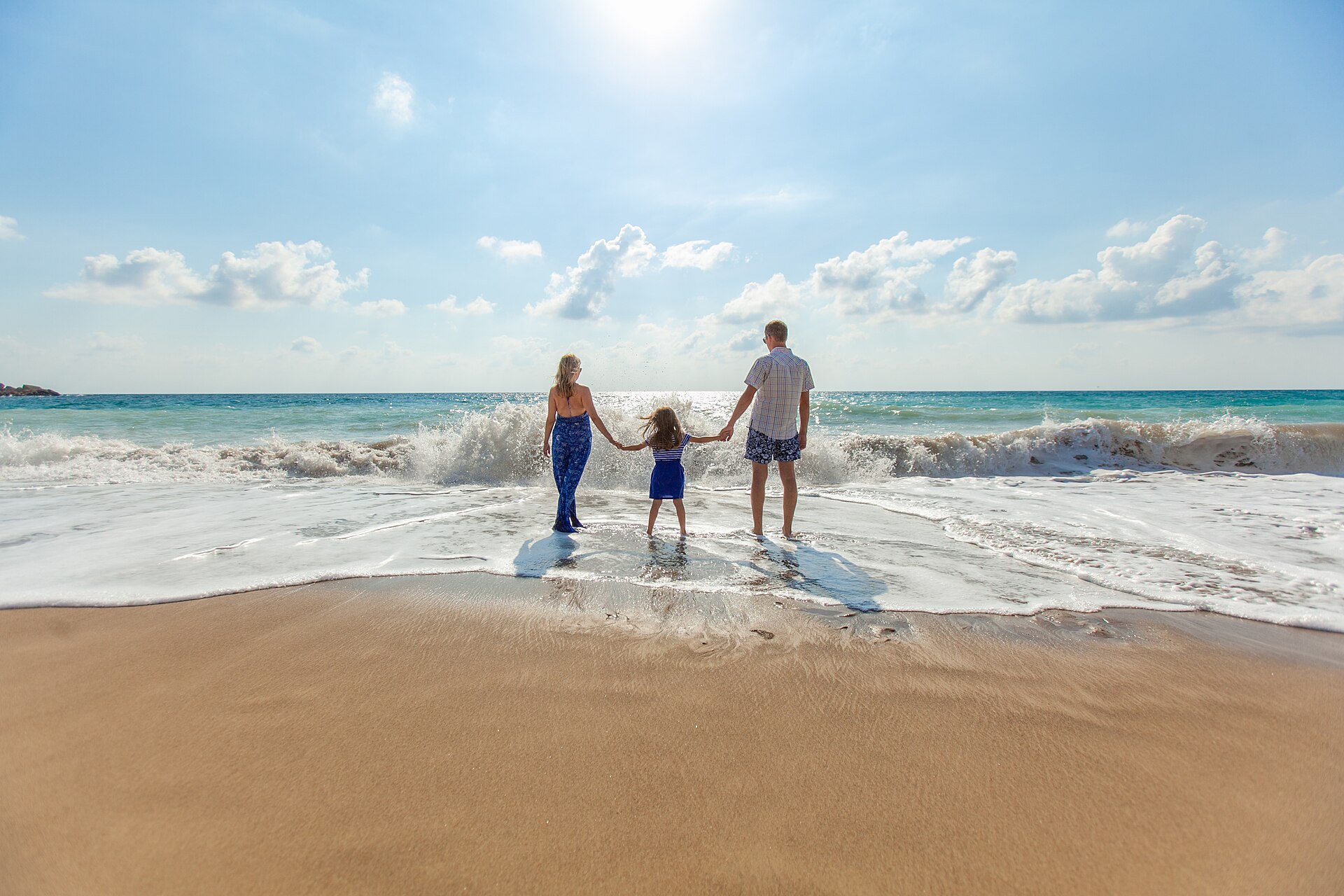 Eine Familie geht Hand in Hand am Strand in die Brandung