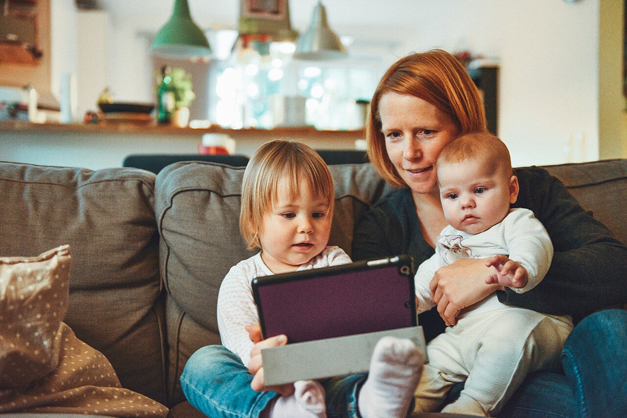 Eine Mutter sitzt mit zwei kleinen Kindern und einem Tablet auf dem Sofa