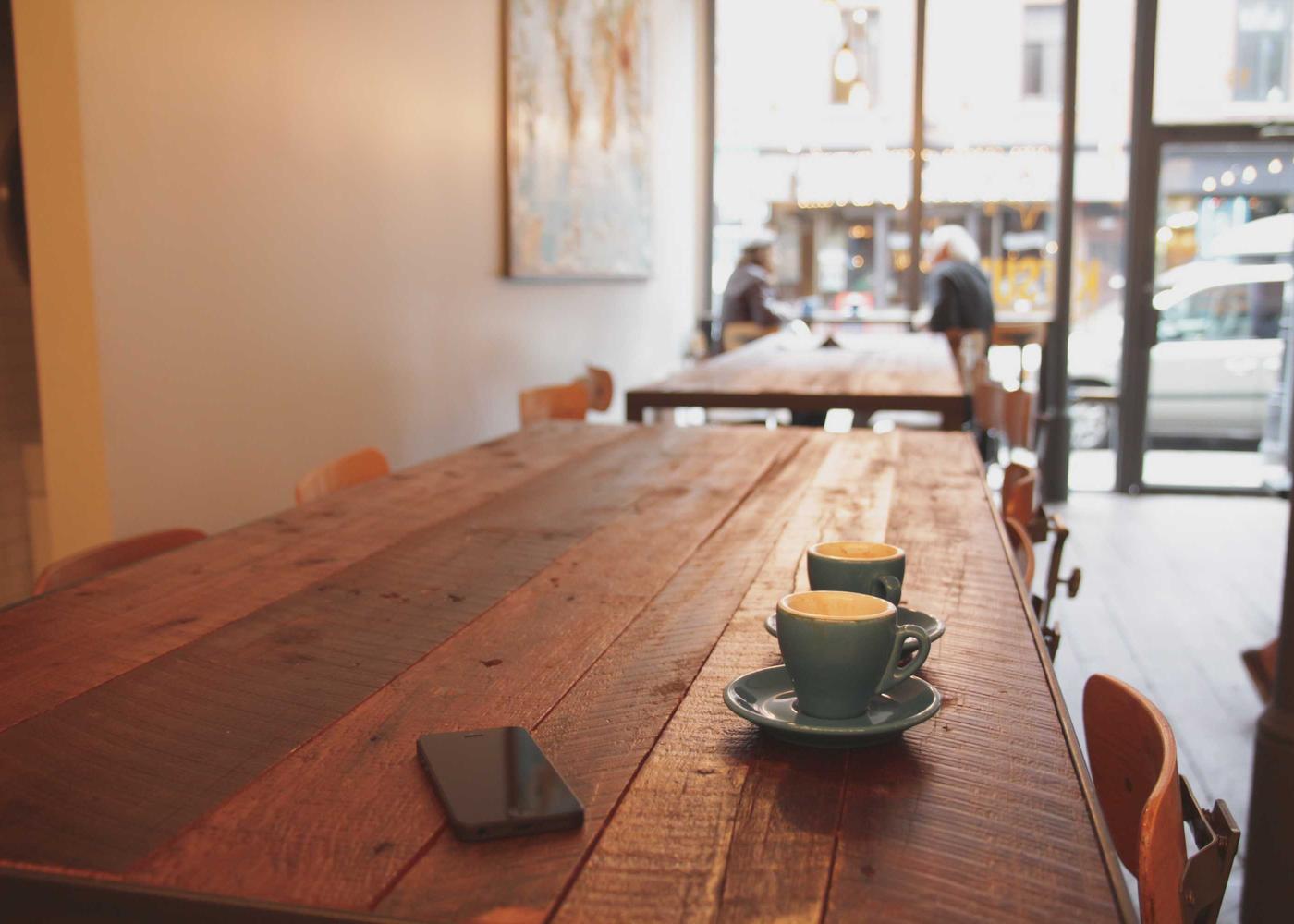 Zwei Kaffeetassen auf einem langen Holztisch in einem hellen Café