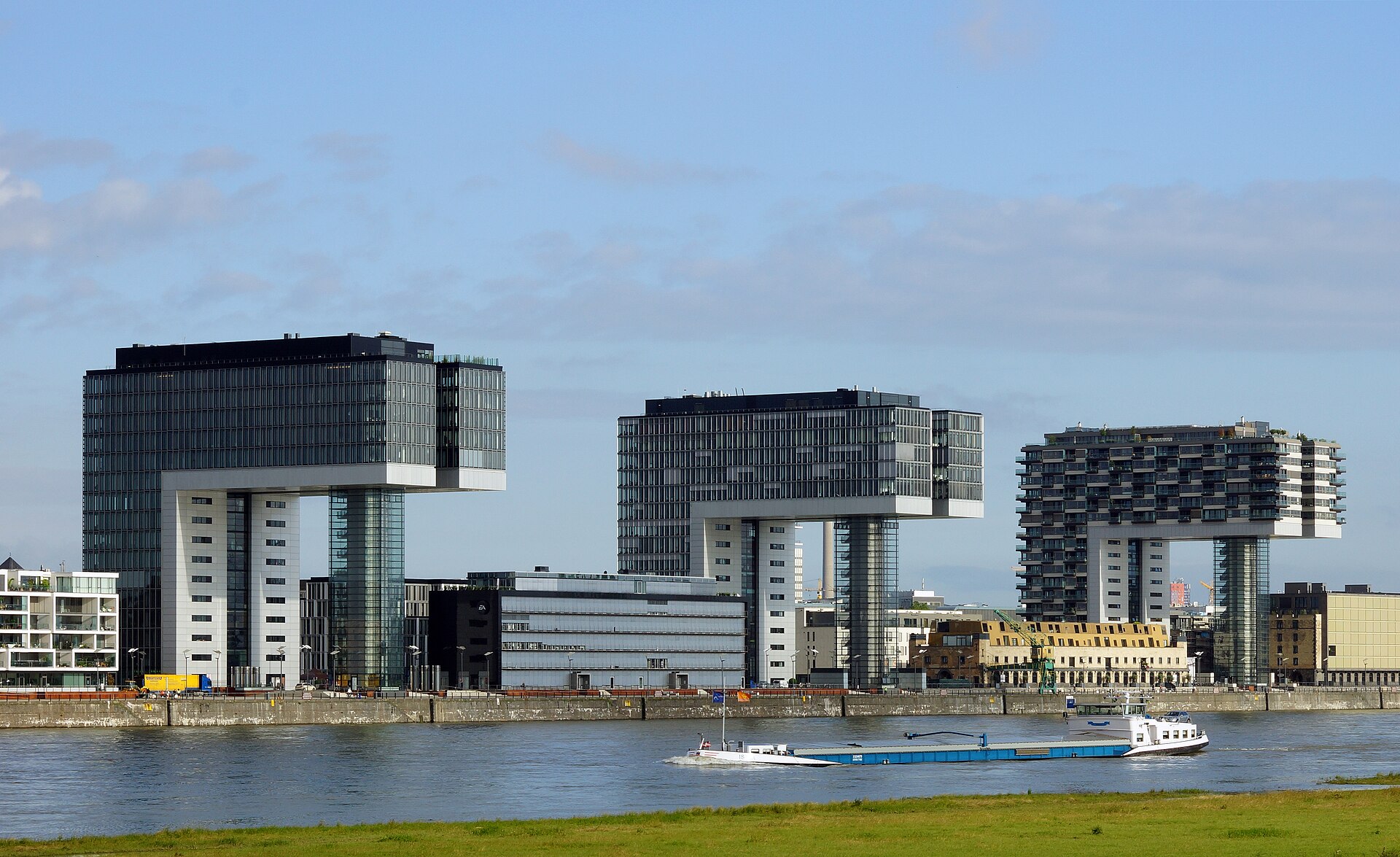 Die drei Kranhäuser am Rheinauhafen in Köln, davor der Rhein mit einem Frachtschiff