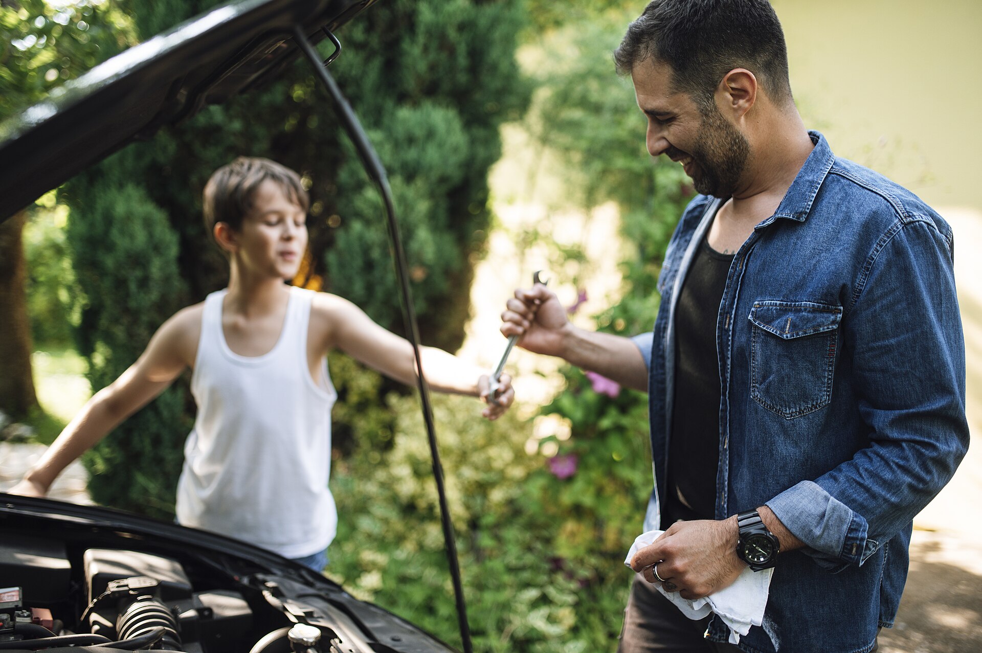 Vater und Sohn schauen gemeinsam unter die geöffnete Motorhaube im Garten