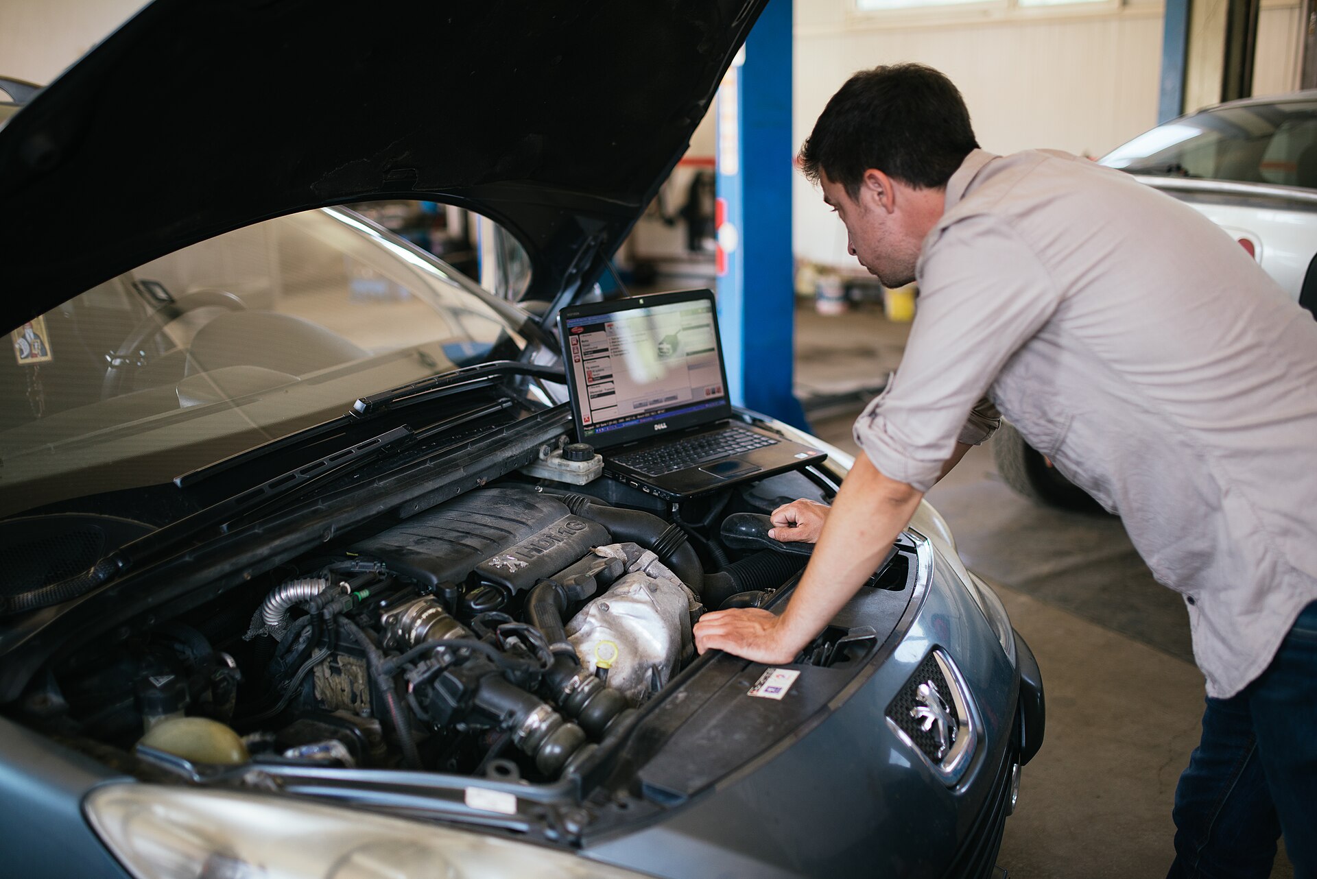 Mechaniker liest in einer Werkstatt mit dem Laptop die Fehler eines Autos aus