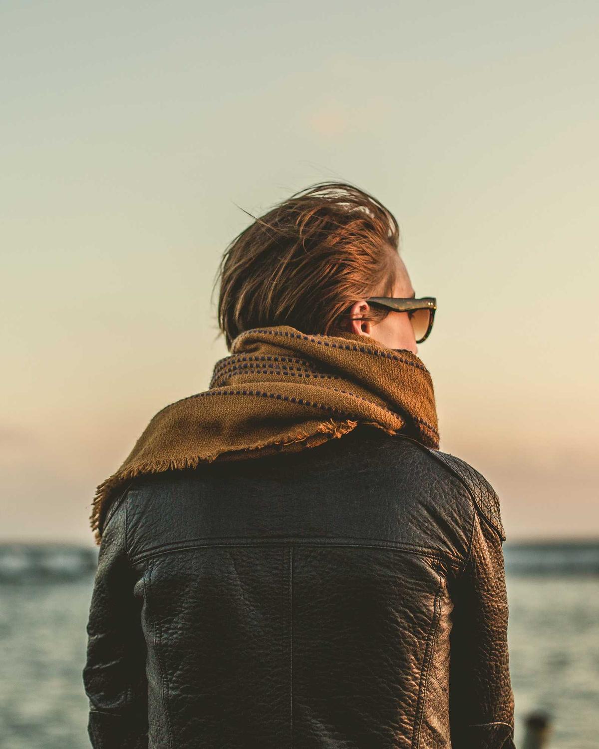 Person mit Schal blickt in der Abendsonne aufs Meer