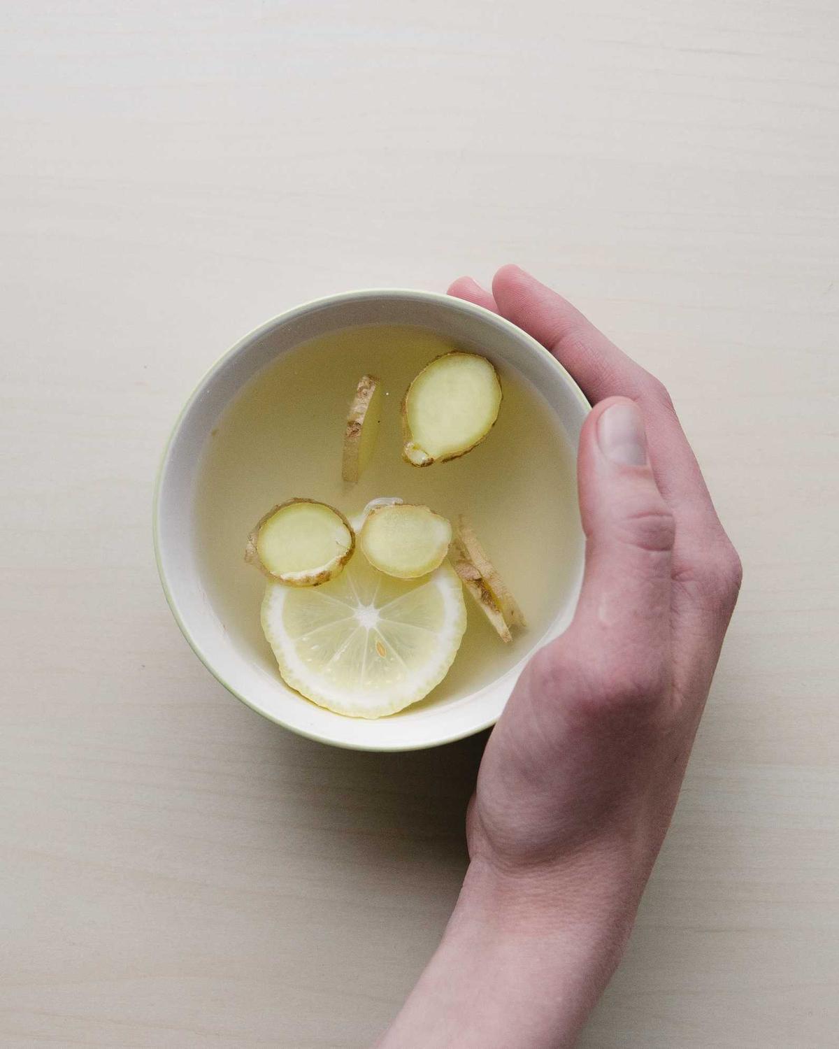 Hand hält eine Schale mit heißem Zitronenwasser